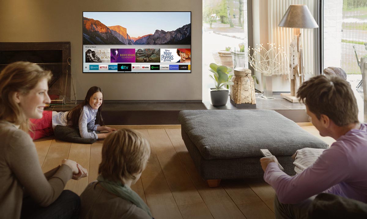 alcune persone, genitori e figli, in salotto guardano lo schermo della smart tv Samsung